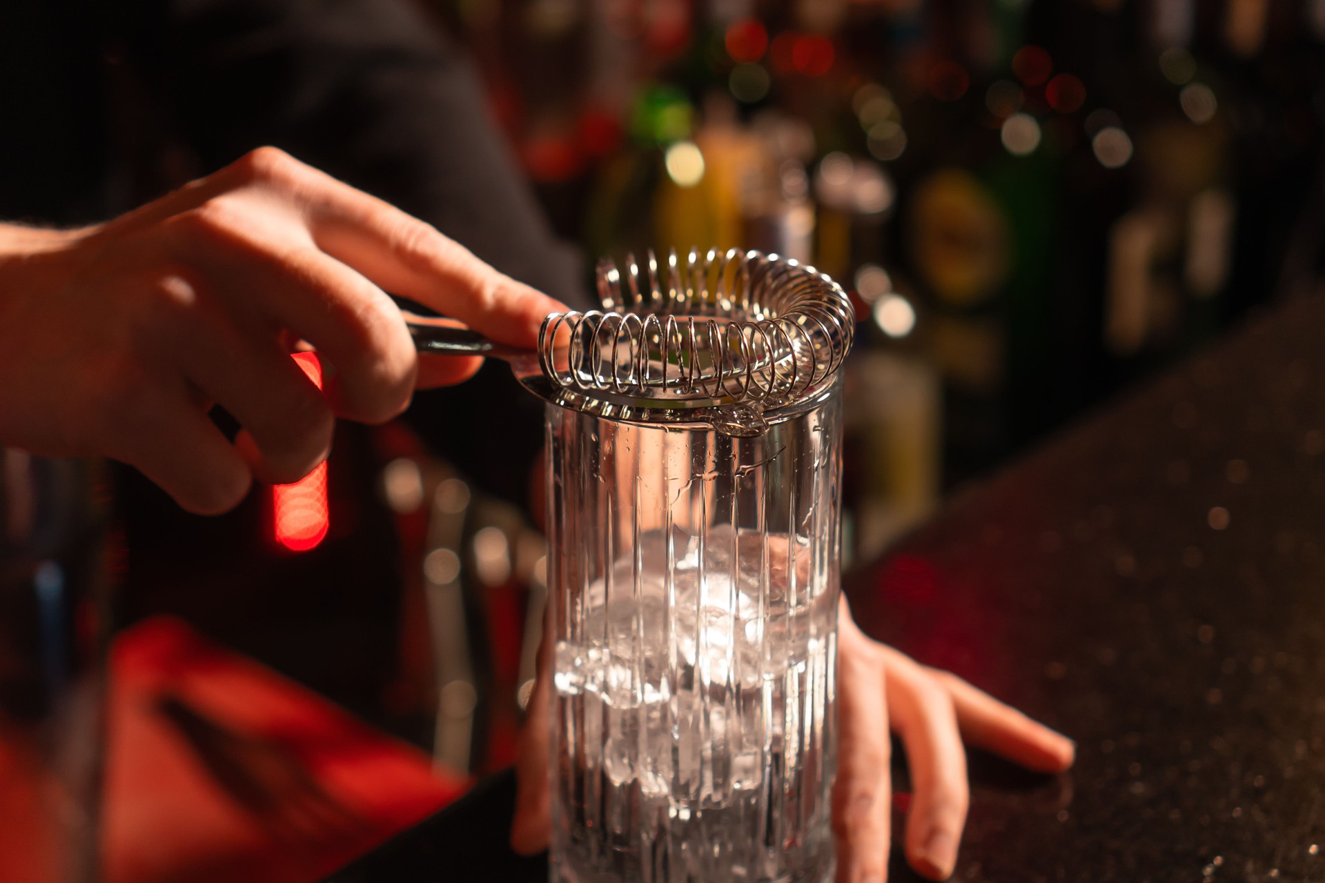 Close-up of the bartender installed a strainer on an ice glass standing on the bar counter. Concept of making cocktails
